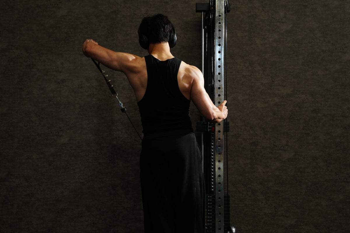 Person performing a lateral raise on a cable tower against a dark background