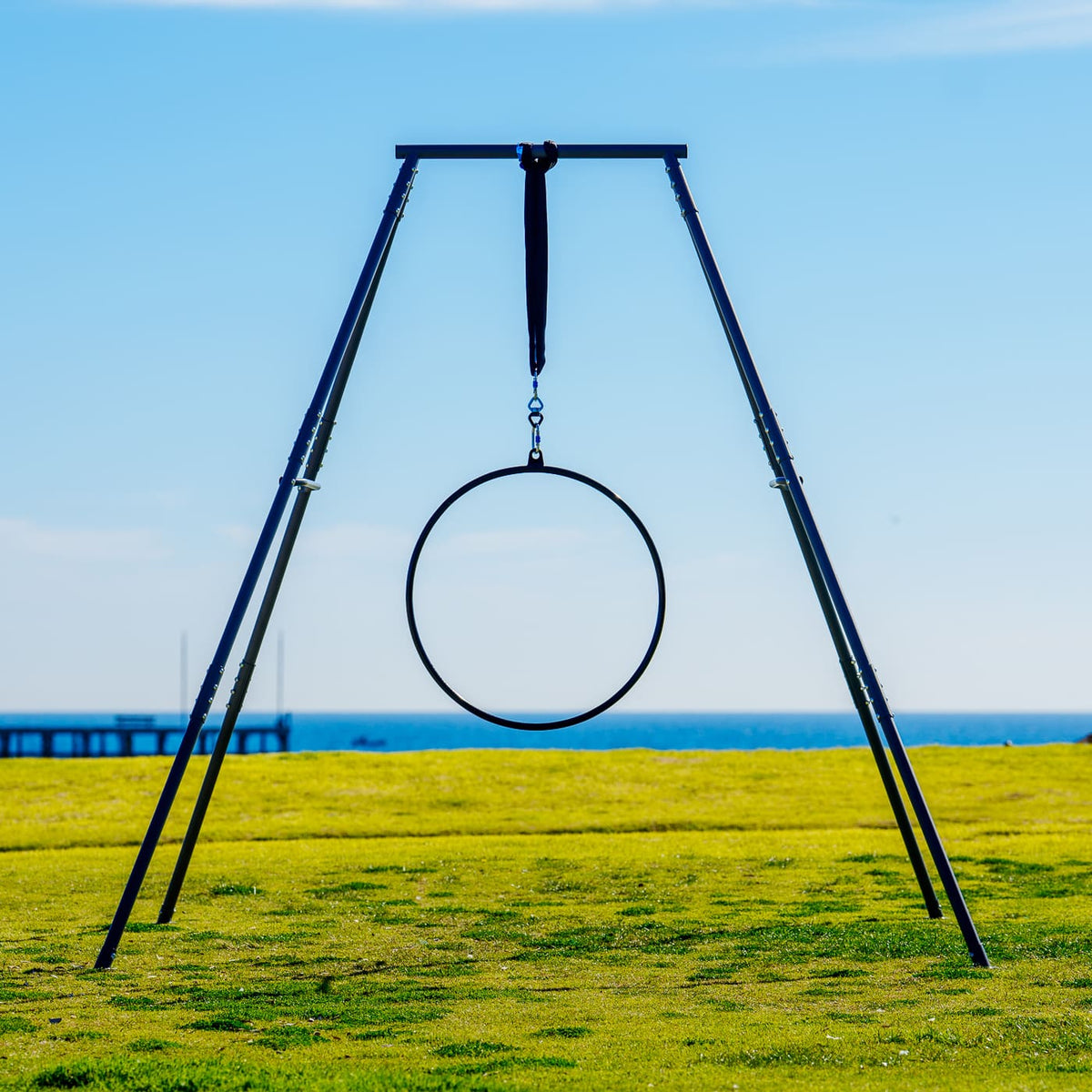 Aerial hoop swing set on a grassy field with a clear blue sky.