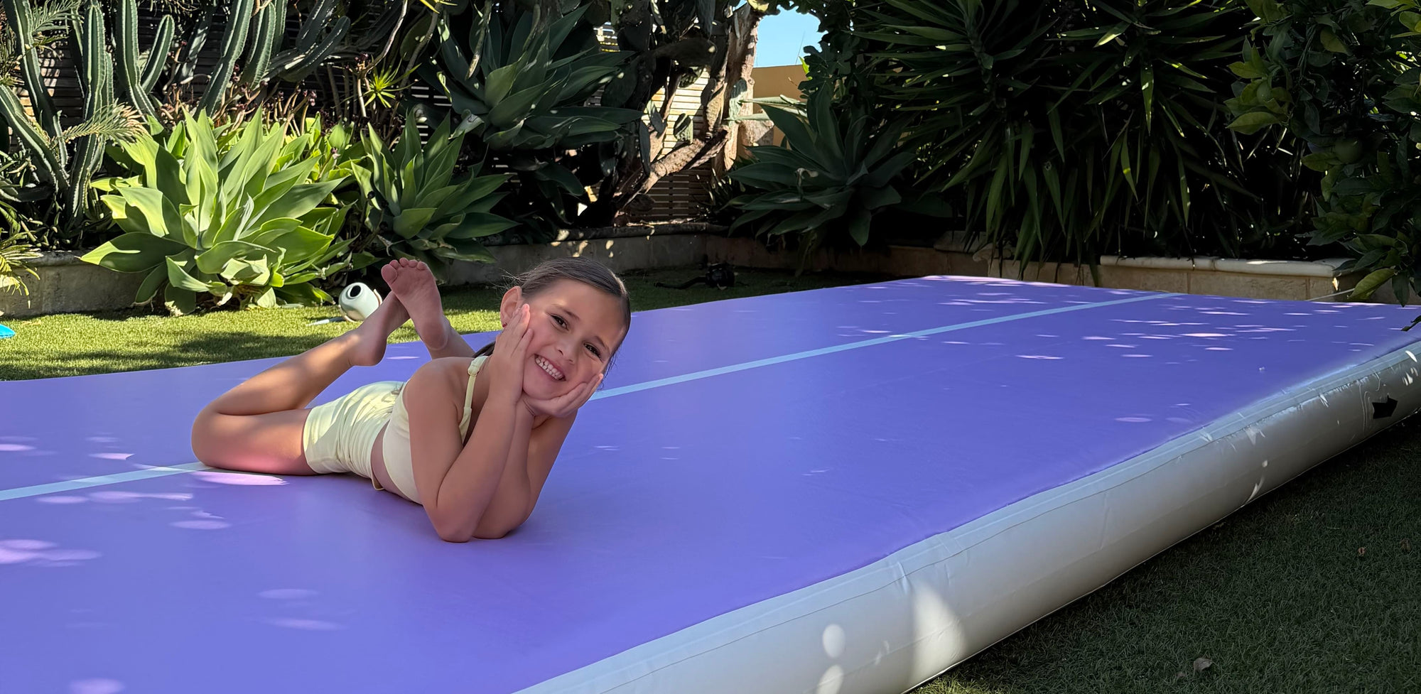 Child lying on a large inflatable airtrack outdoors with greenery in the background