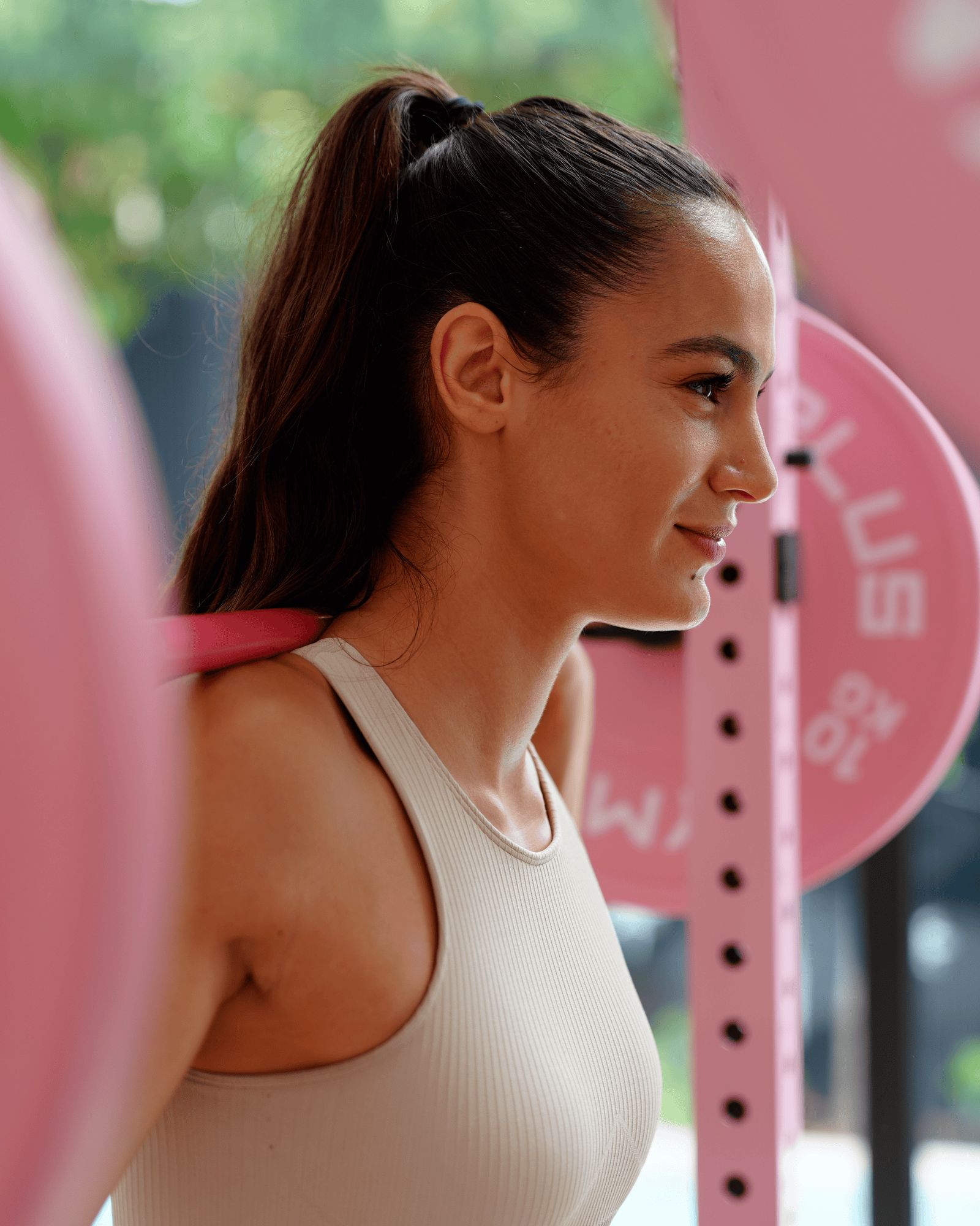 Woman in a beige tank top standing outdoors with pink equipment in the background