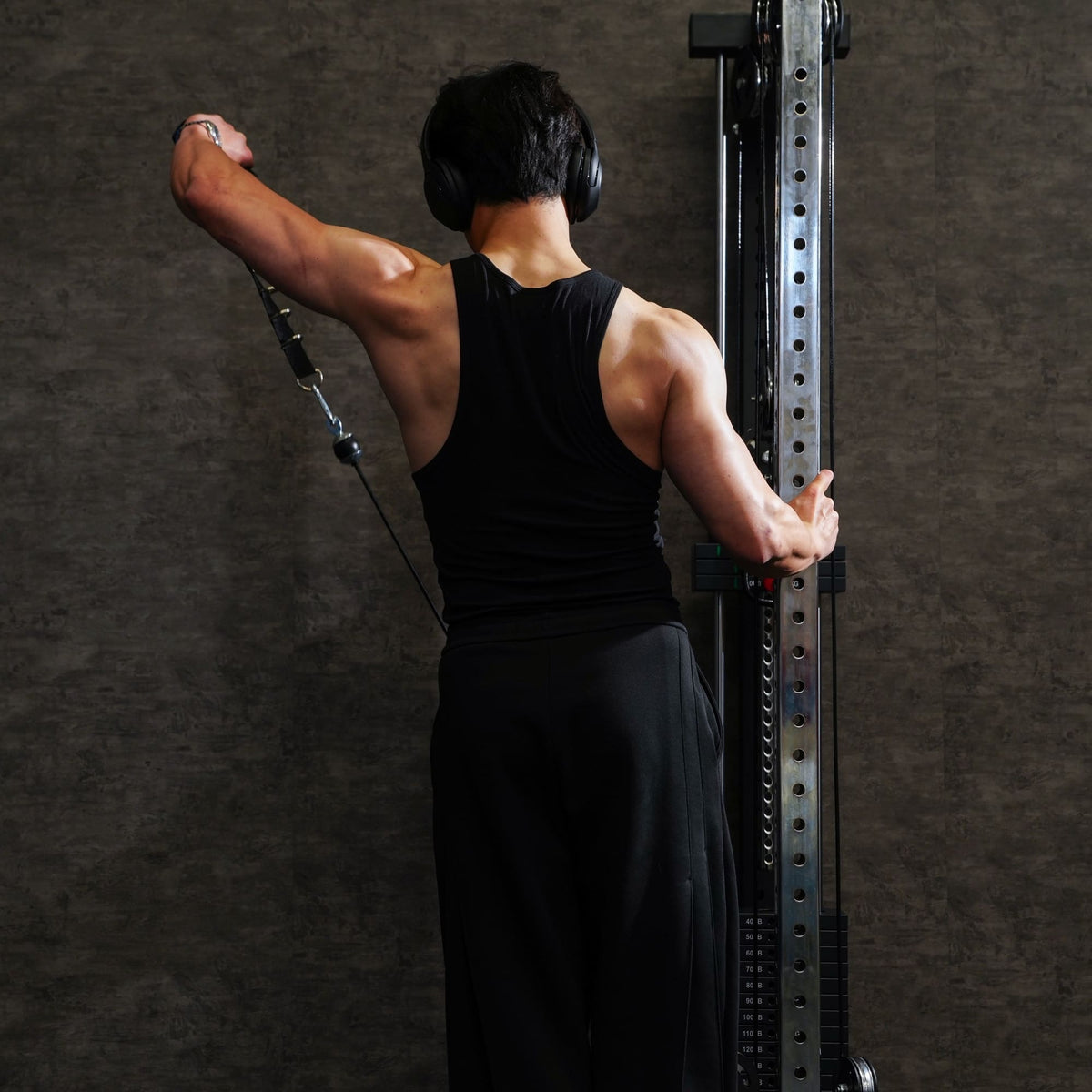 Person in black tank top and pants using a cable tower against a dark background